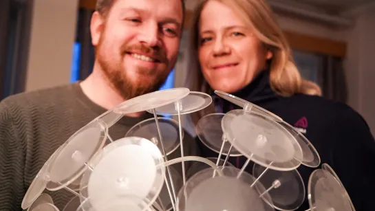Two people indoors hold a cluster of clear plastic suction cups on rods, forming a dome-like display.