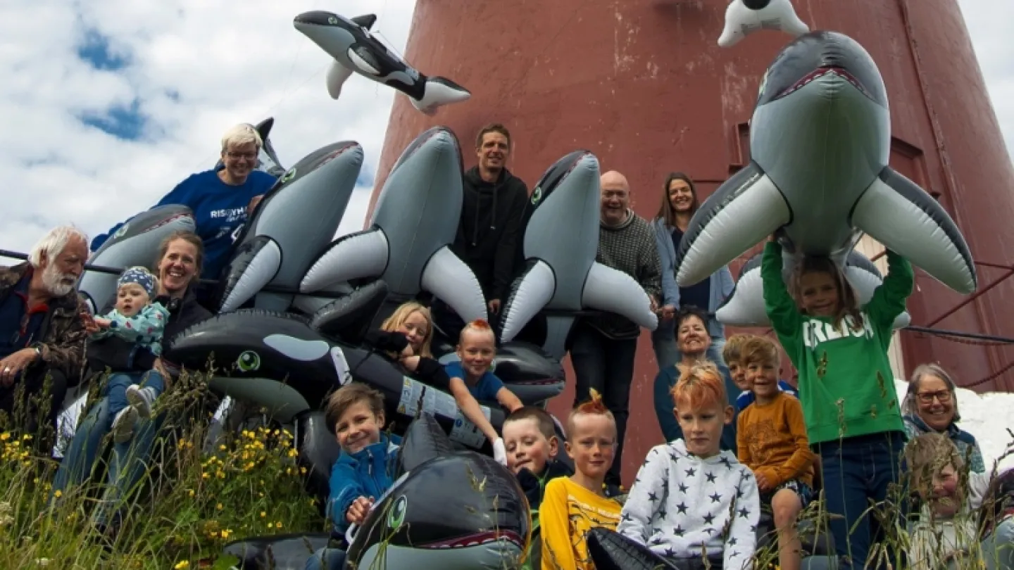 Low-angle view of a tall red lighthouse with many inflatable whales and sharks piled below under a cloudy sky.