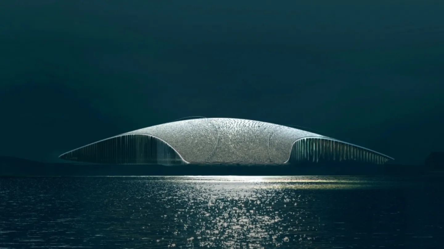 Low futuristic dome-shaped building spans calm water at night, with shimmering reflections beneath a dark sky.