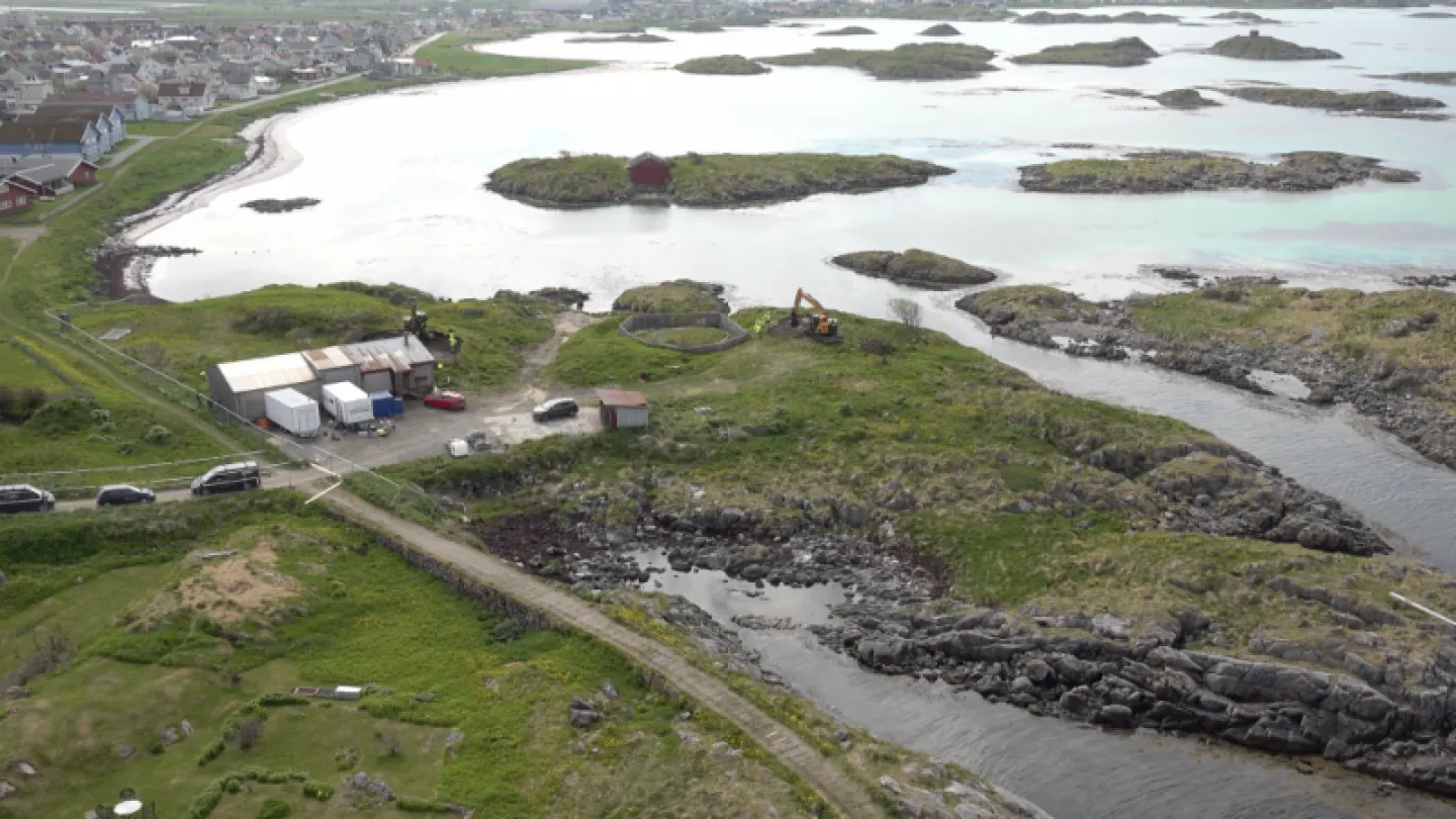 Aerial view of rocky coastline with grassy land, small islands, a lagoon, and a roadside worksite with vehicles.
