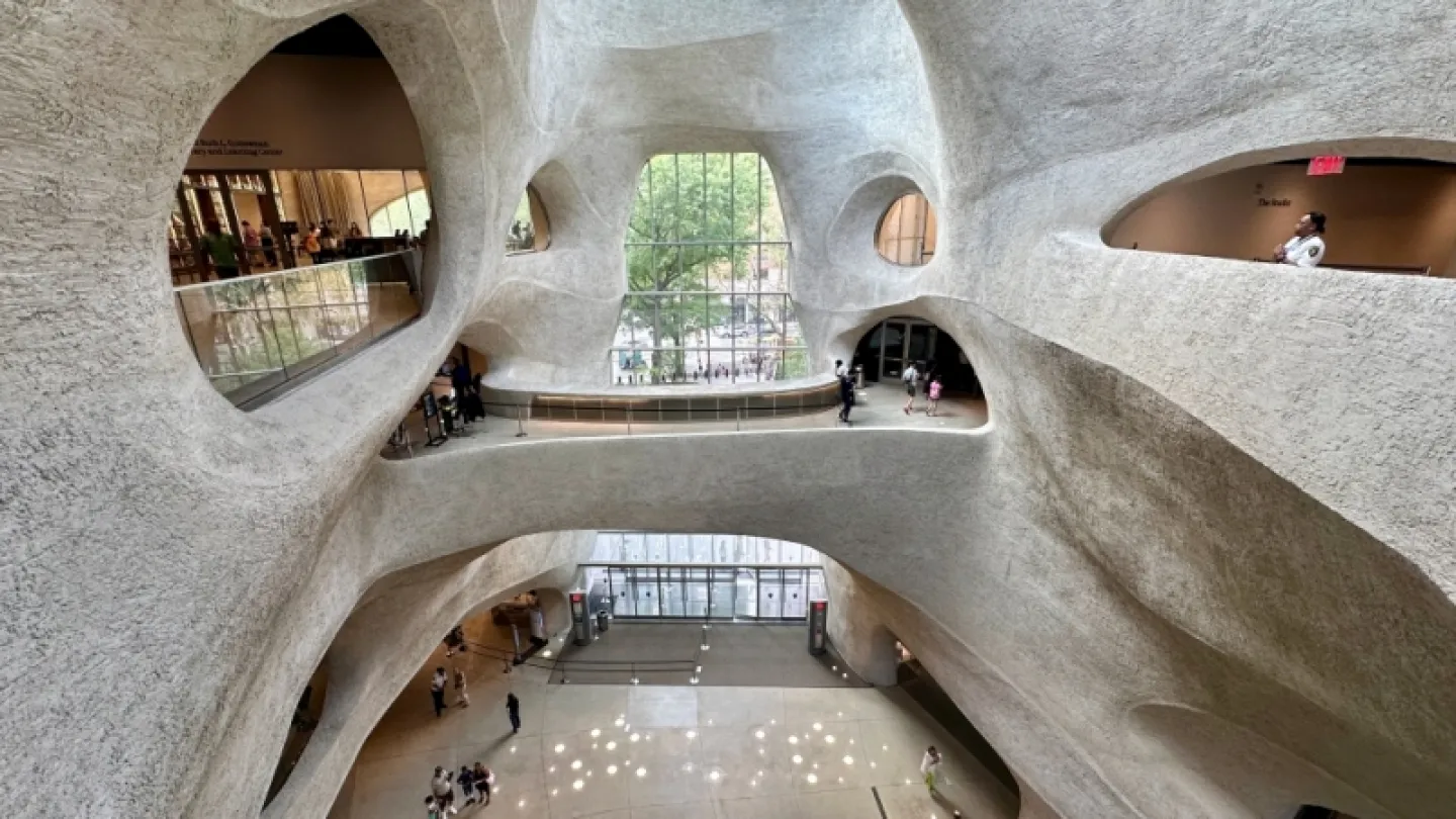 Interior atrium with sculpted concrete walls, oval openings, walkways, and people across multiple levels.