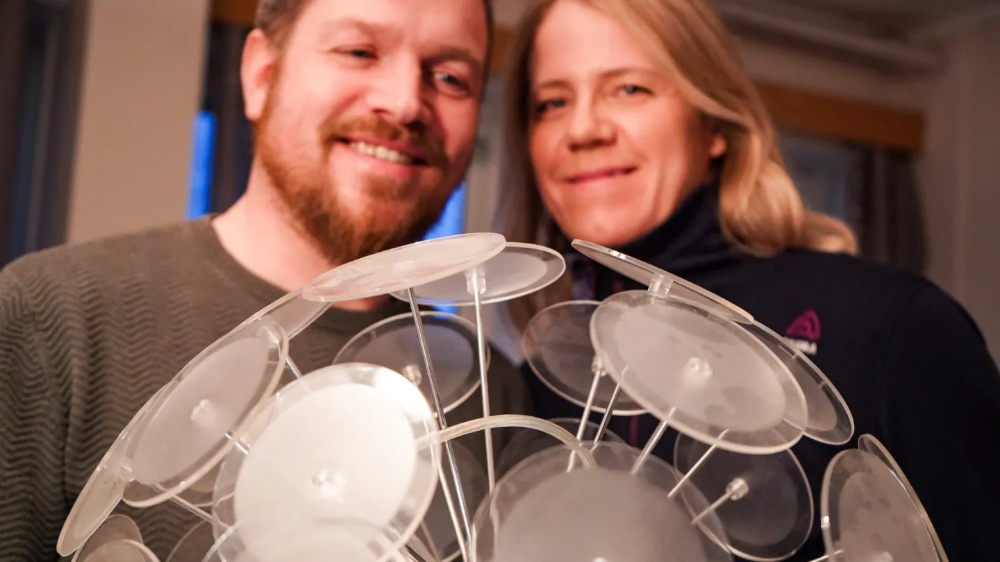 Two people indoors hold a cluster of clear plastic suction cups on rods, forming a dome-like display.