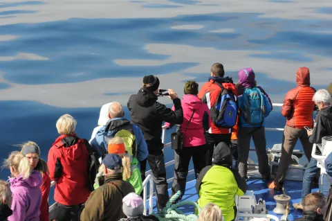 Group of people in colorful jackets and backpacks stand on a boat deck, looking out over icy blue water.