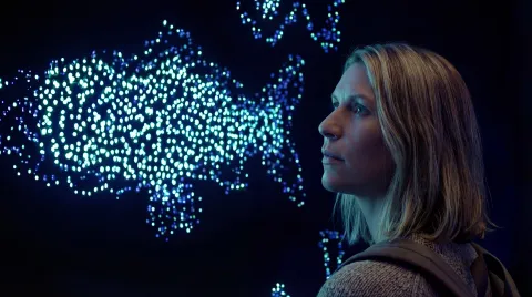 Person with shoulder-length hair and a backpack looks at a glowing dot-based world map display in a dark room.