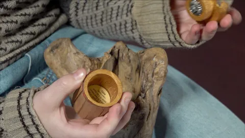 Close-up of hands in a knit sweater holding small wooden containers on denim jeans beside a piece of driftwood.