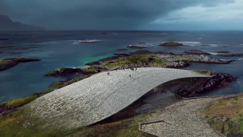 A sweeping curved stone roof on a coastal hill, with people walking above turquoise sea and rocky islets under dark clouds.